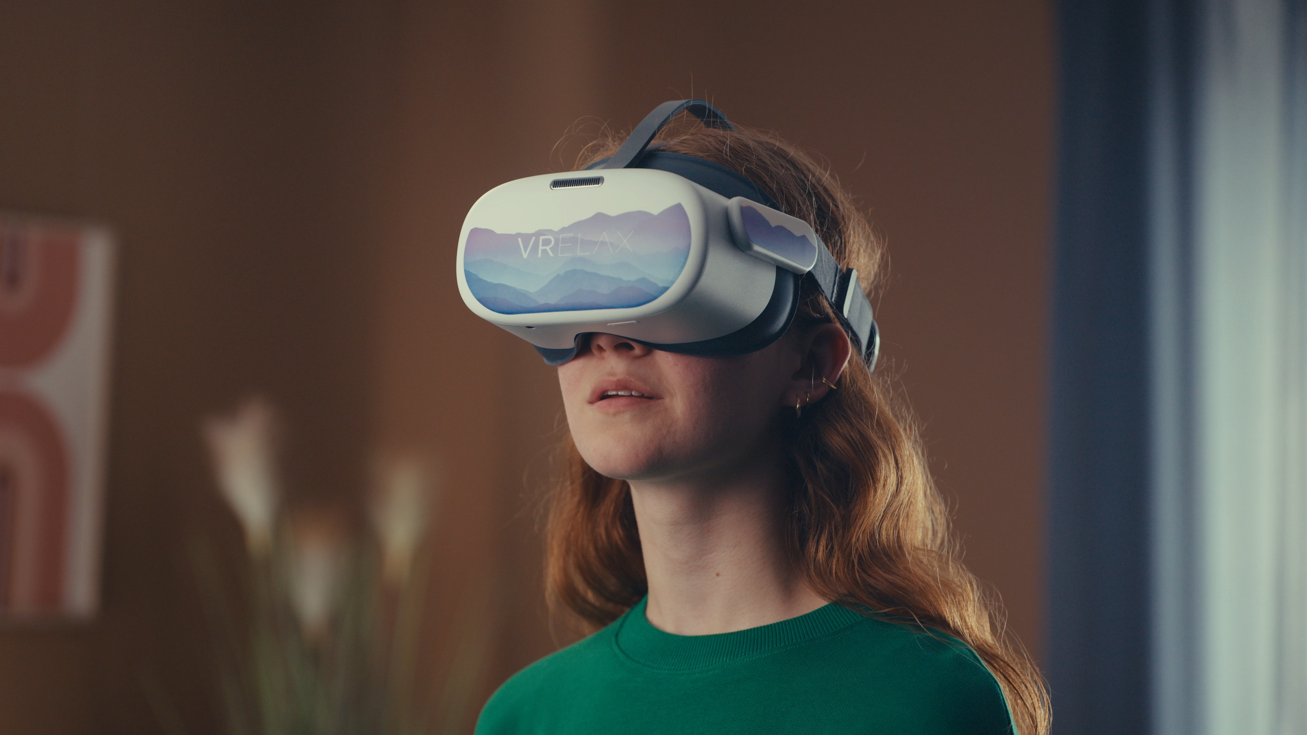 A young woman wearing a virtual reality (VR) headset in domestic surroundings, taken from Sensu.health's commercial video for VRelax