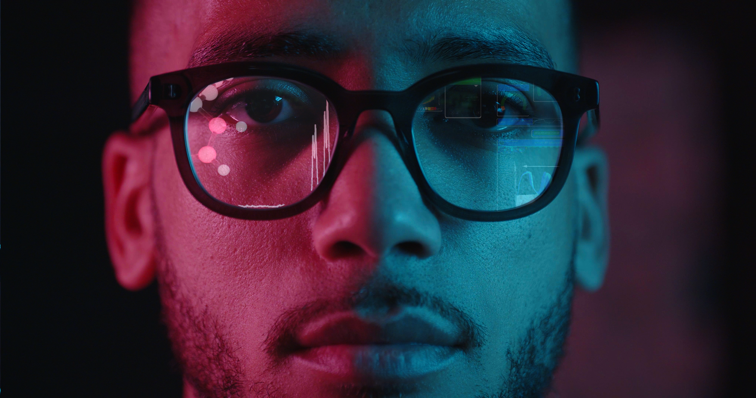 The face of a person wearing glasses with superimposed NMR radiofrequency waves in pink, red and blue studio lighting, taken from our video on Bruker's Fourier PAT benchtop NMR system